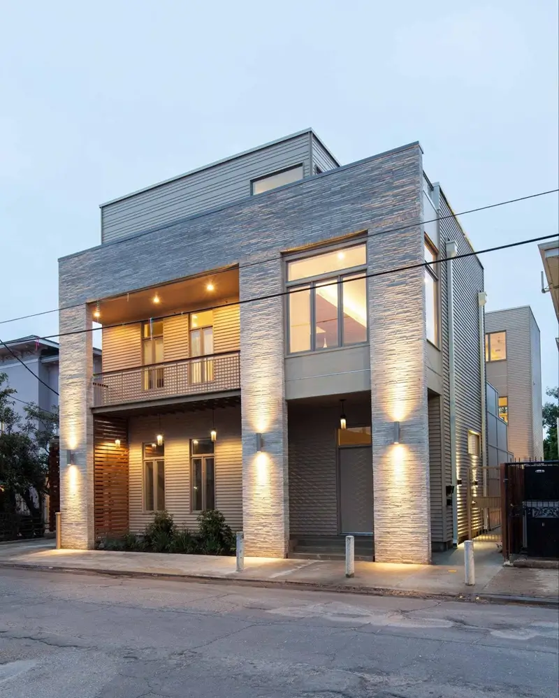 A contemporary house illuminated to showcase its modern architectural design with a spacious front porch and a driveway