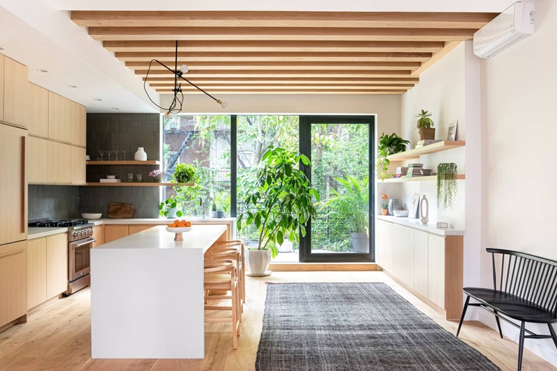 A sunlit kitchen featuring wooden accents, a black floor rug, an open window, and plants bathed in warm light