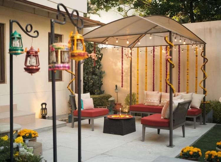 Diwali Decoration Items A charming outdoor area featuring a small gazebo with seating chairs, adorned with fairy lights, garlands, and lanterns hanging from the poles.