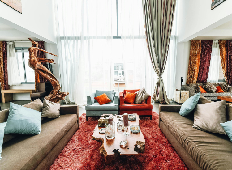 Living room interior featuring a red fluffy rug, stylish chairs and sofas, with ample natural light streaming through a large window.